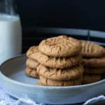 Grey plate with a pile of vegan gluten-free peanut butter cookies on it next to a glass of milk.