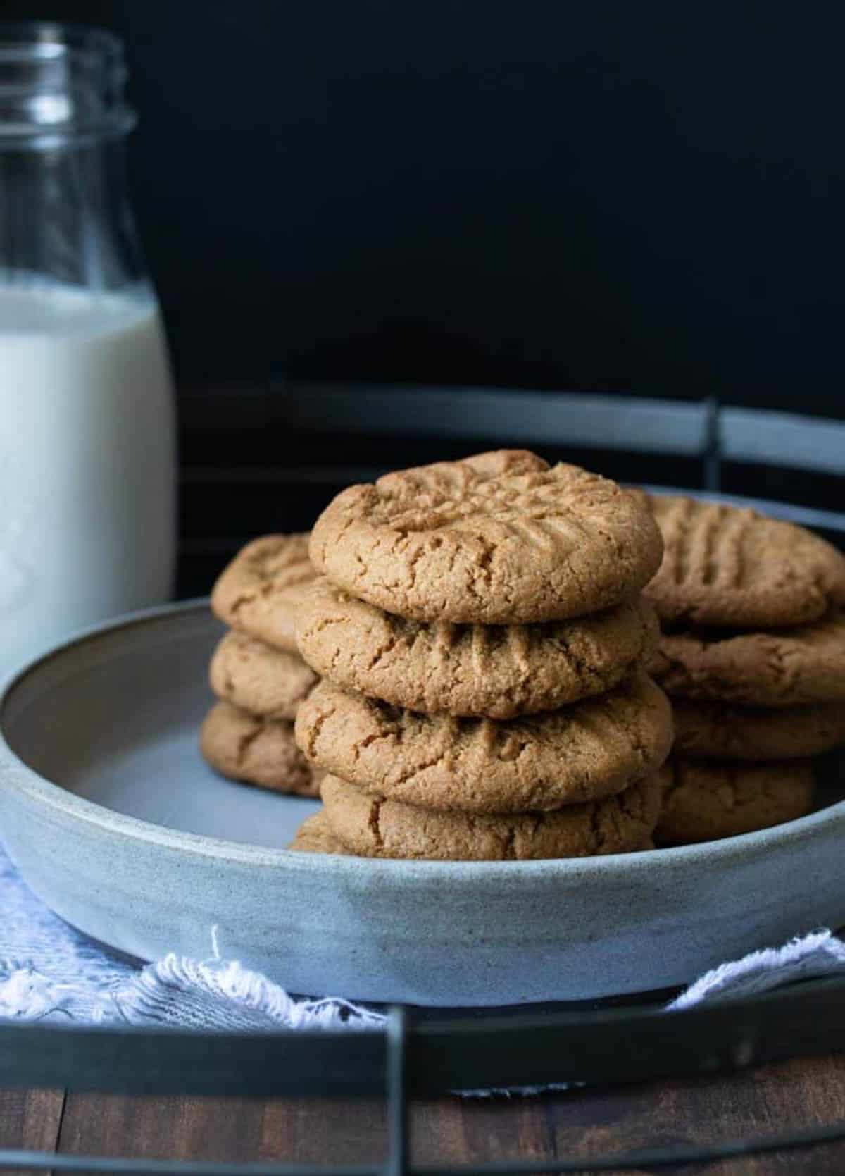 Grey plate with a pile of vegan gluten-free peanut butter cookies on it next to a glass of milk.