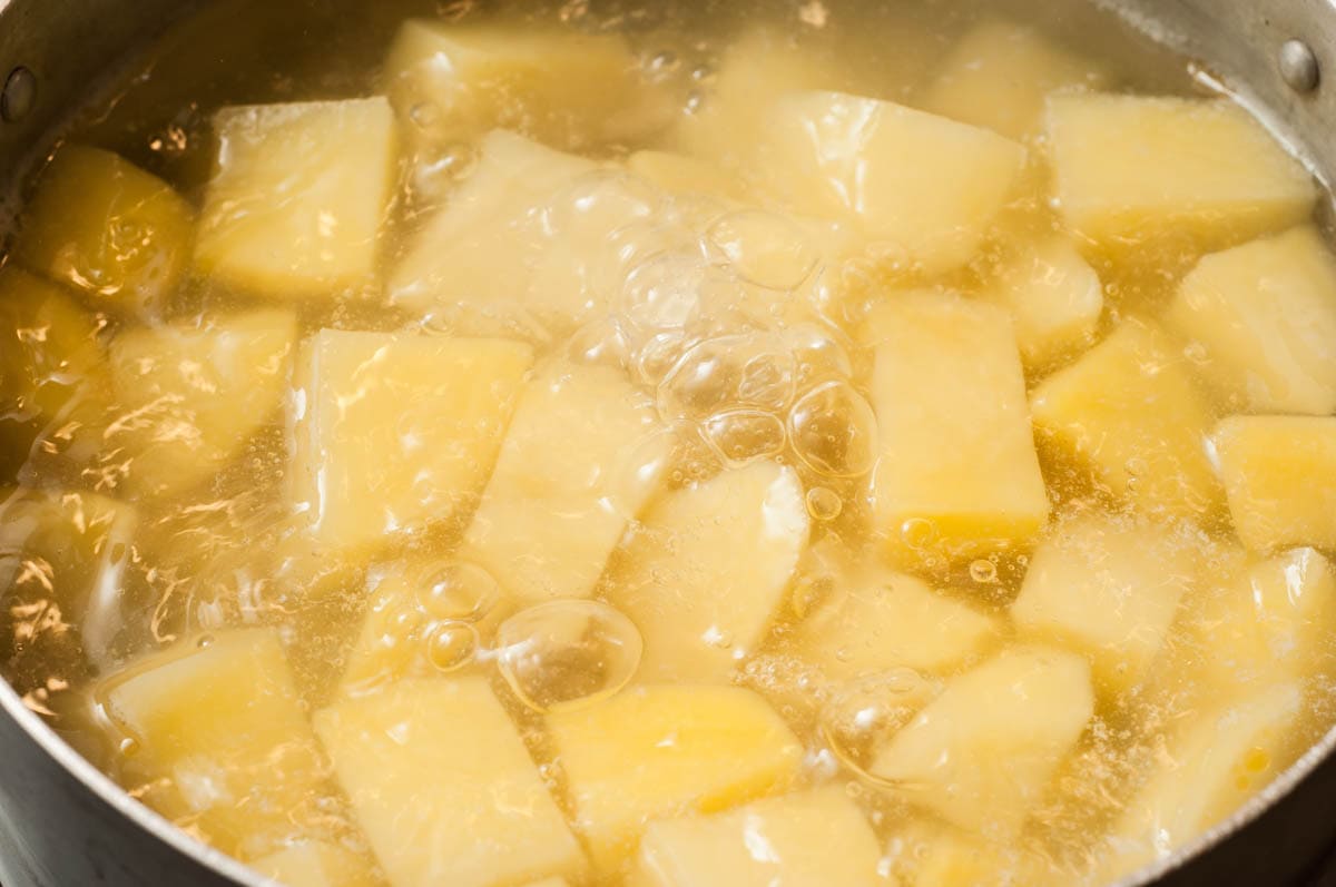 Potato cubes boiling in water in a large pot on the stove.