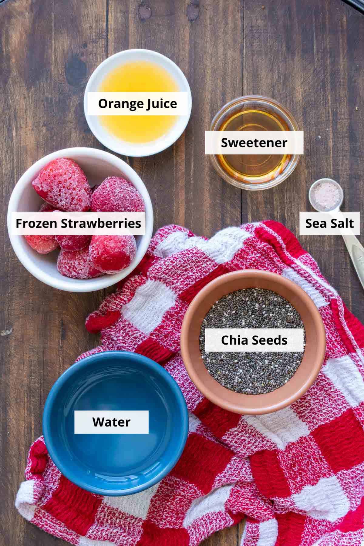 Colored bowls with ingredients to make strawberry chia seed jam on a red checkered towel.