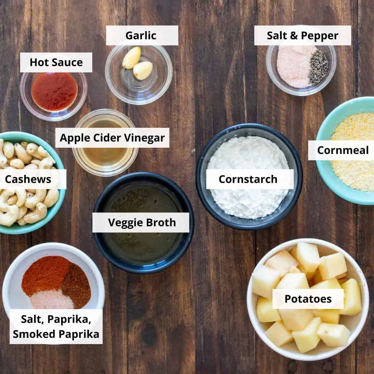 Bowls with cubed potatoes, cornmeal, cornstarch, salt and pepper, paprika, hot sauce, garlic, cashews, broth, and apple cider vinegar