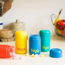 Hiya vitamins bottles displayed on a countertop with some bottles open and some tablets on the countertop.