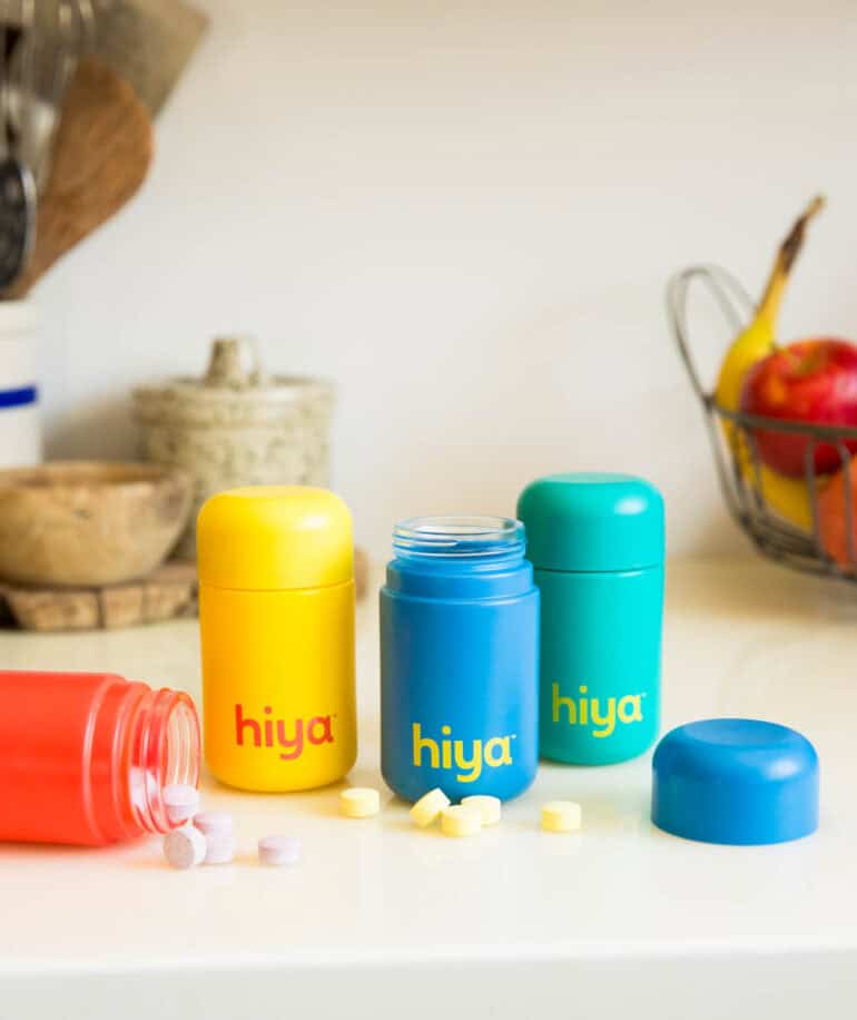 Hiya vitamins bottles displayed on a countertop with some bottles open and some tablets on the countertop.