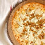 Pear and gorgonzola pizza with walnuts served on a wood cutting board.