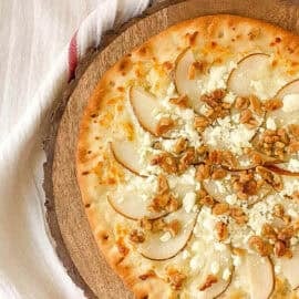 Pear and gorgonzola pizza with walnuts served on a wood cutting board.