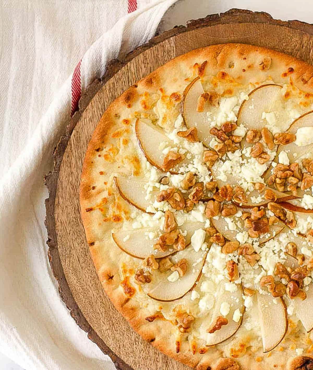 Pear and gorgonzola pizza with walnuts served on a wood cutting board.