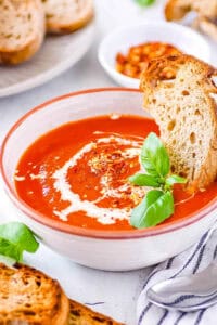 Tomato soup with canned tomatoes served in a white bowl with fresh basil and crusty bread as a garnish.