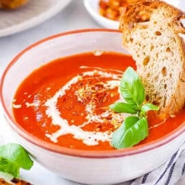 Tomato soup with canned tomatoes served in a white bowl with fresh basil and crusty bread as a garnish.