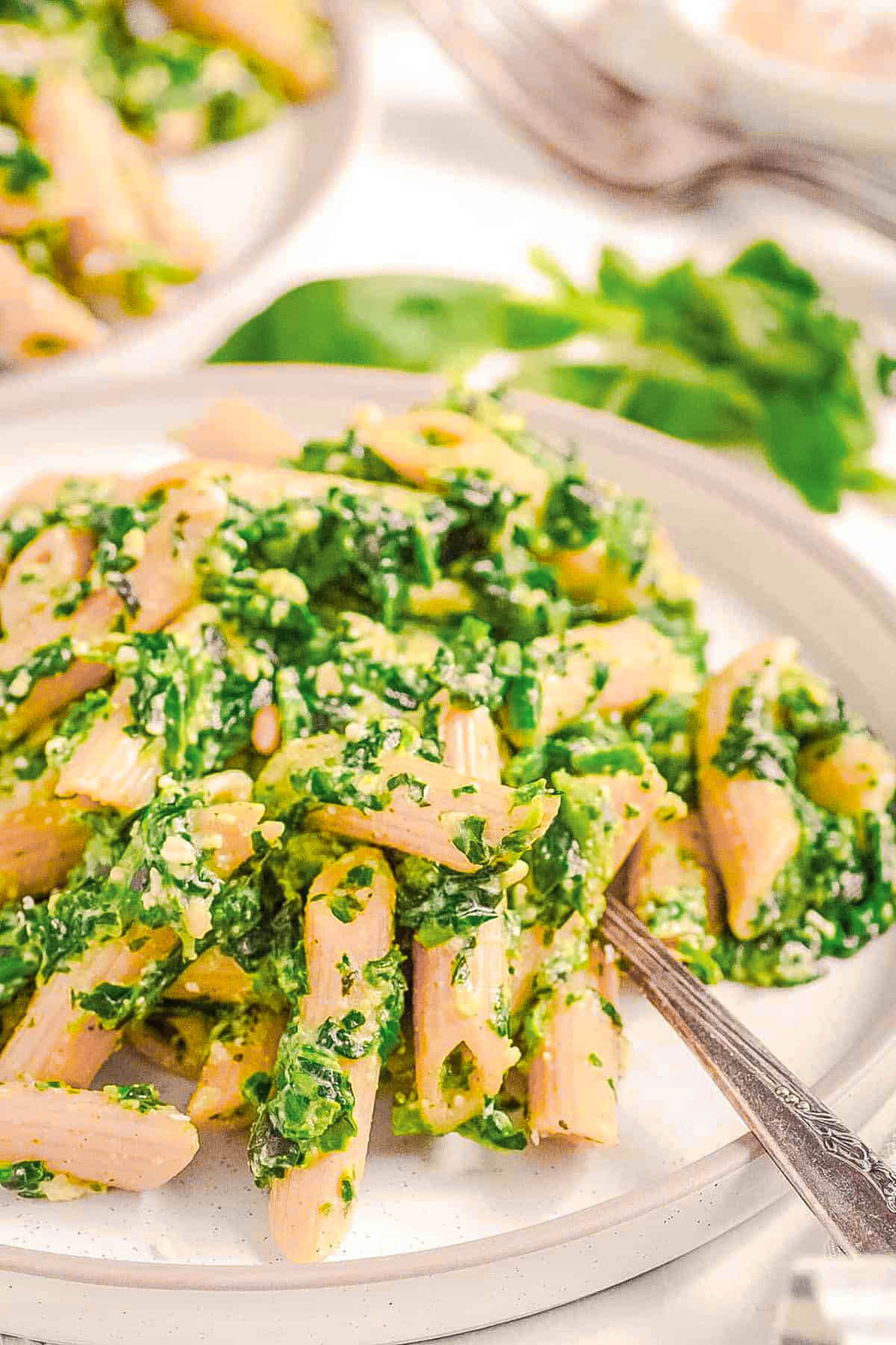 Vegetarian pesto pasta recipe with spinach, basil and pine nuts on a white plate.