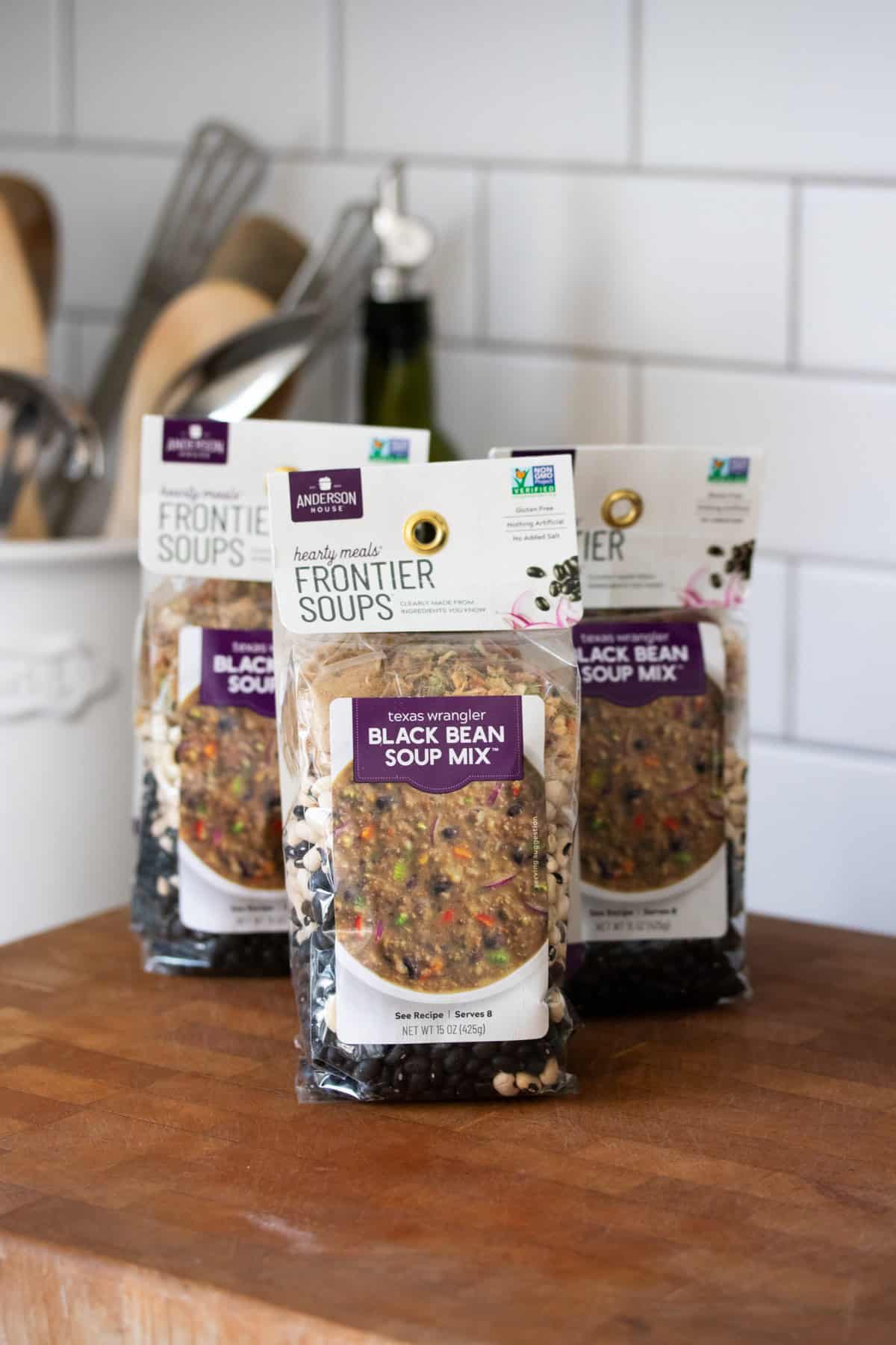 Three bags of black bean soup mix sitting on a wooden surface in a kitchen.