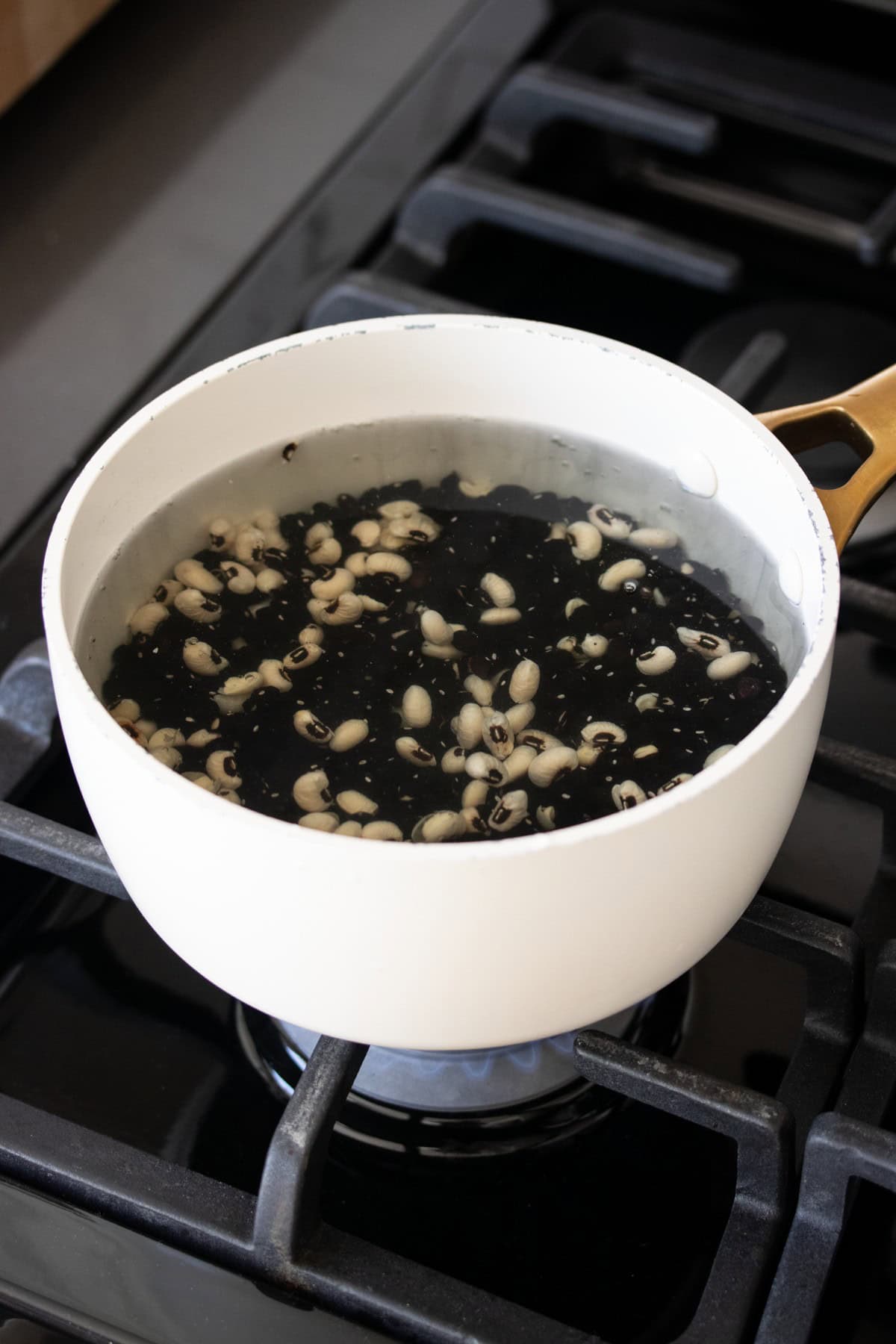 A white pot with black beans and white beans in water on a stove top.