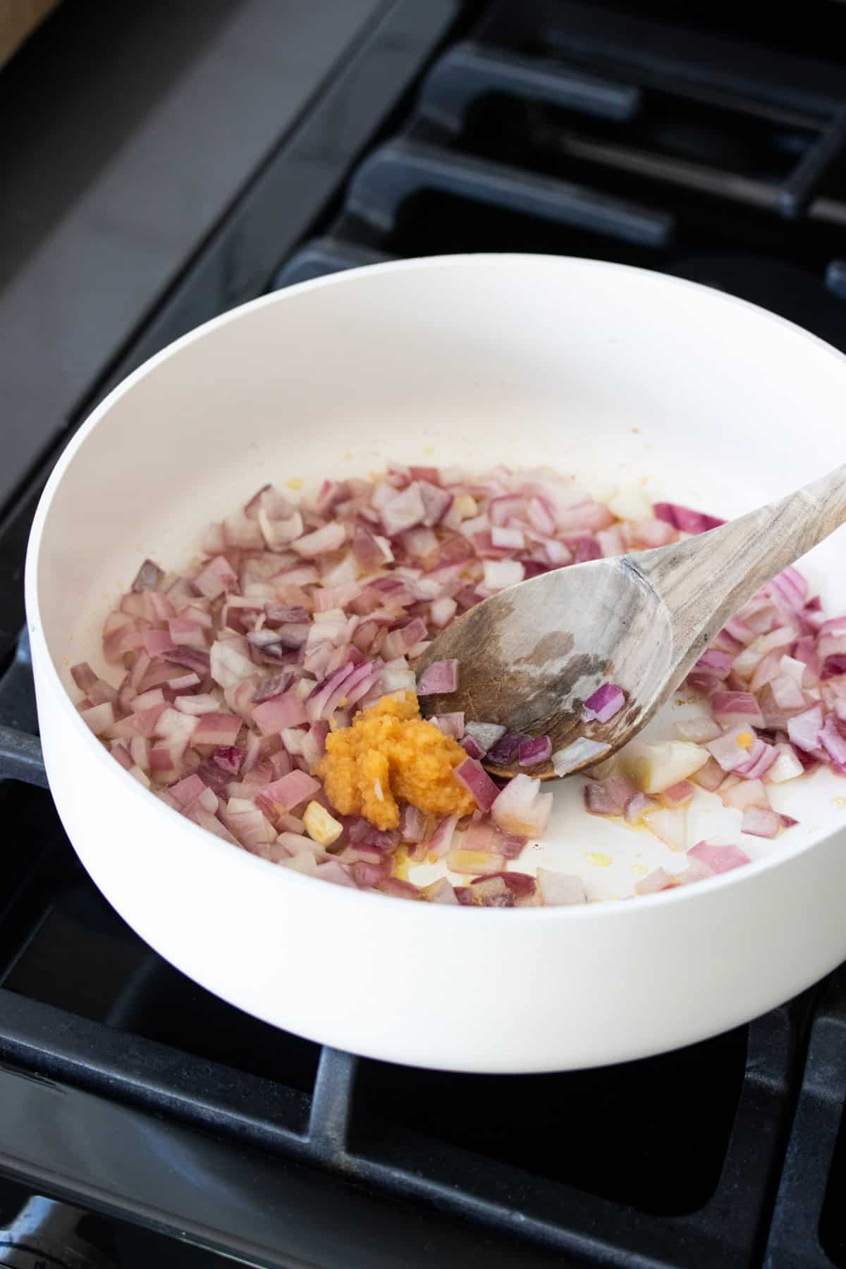 Red onion and garlic being mixed around in a white pan by a wooden spoon.