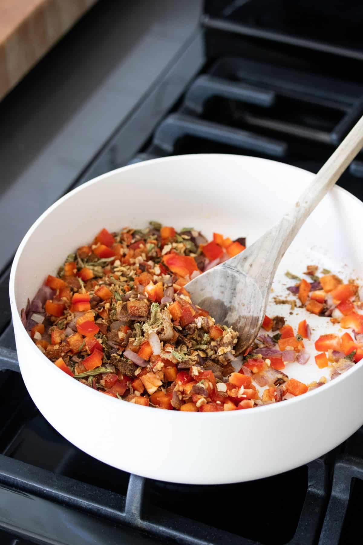 Chopped red peppers with dried soup mix being mixed with a wooden spoon in a white pan.