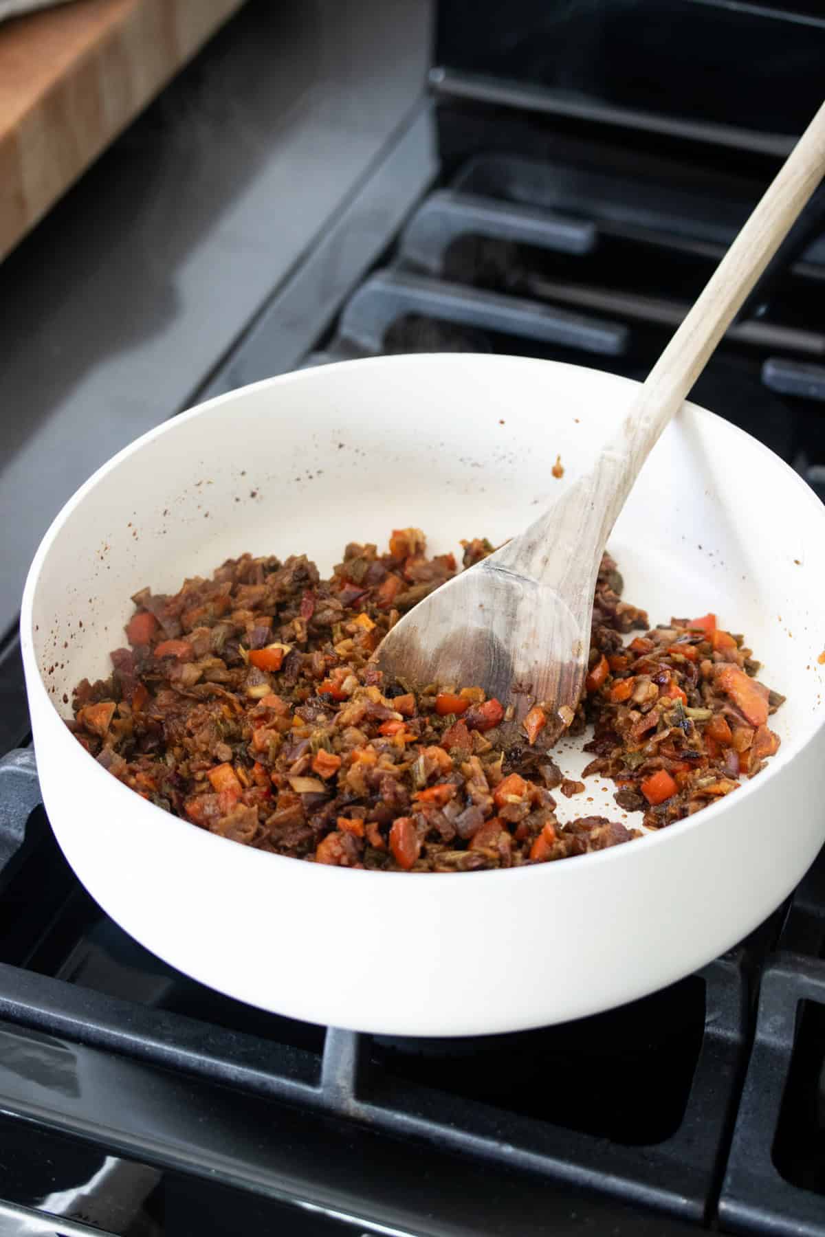 White pan with a pepper and soup mix mixture being mixed around by a wooden spoon.