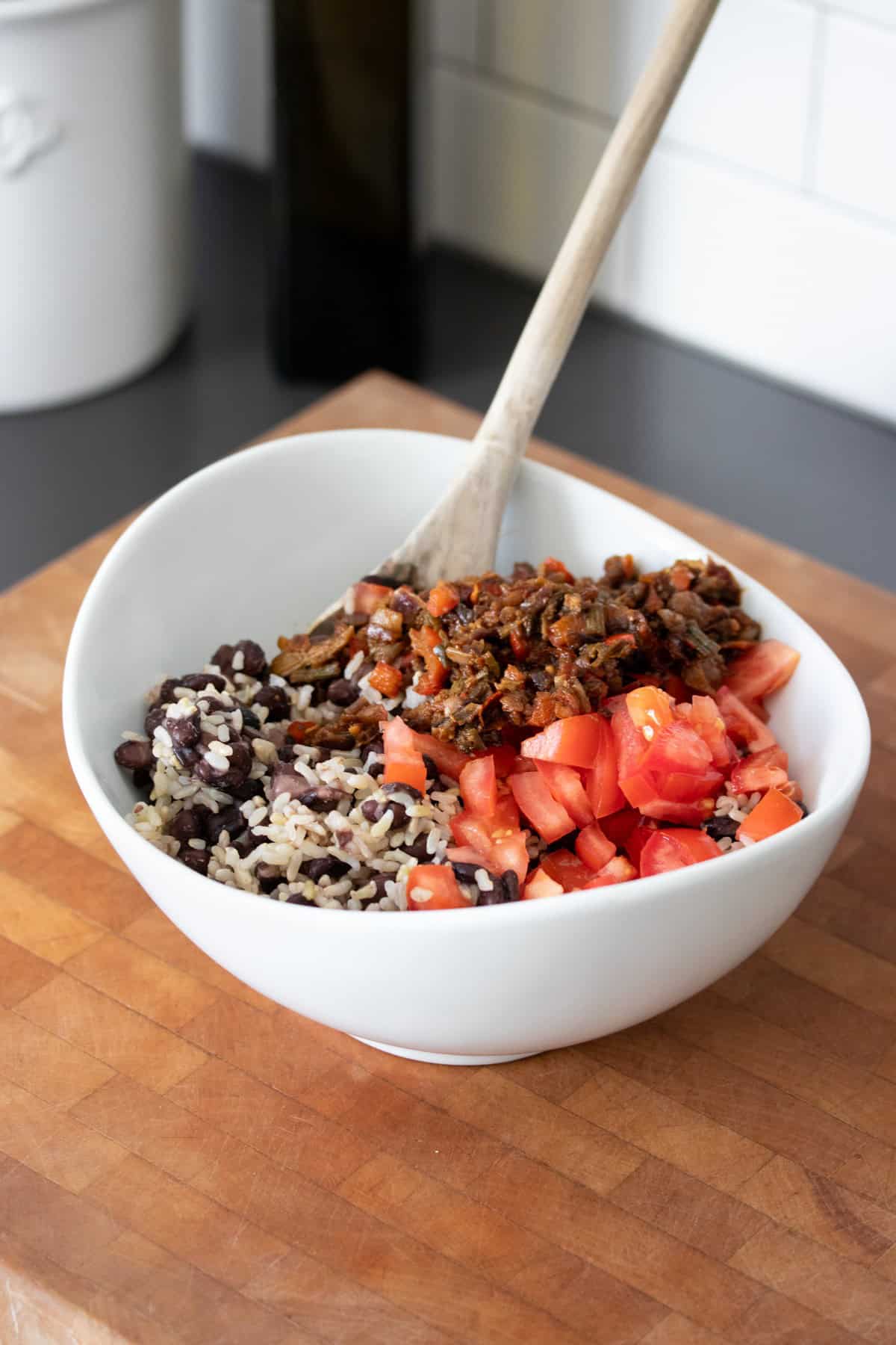 White bowl with a black bean and rice mixture, fresh chopped tomatoes and a cooked soup mix mixture in sections inside.
