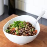 A black bean and rice salad in a white bowl topped with fresh chopped cilantro sitting on a wooden surface.