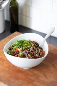 A black bean and rice salad in a white bowl topped with fresh chopped cilantro sitting on a wooden surface.