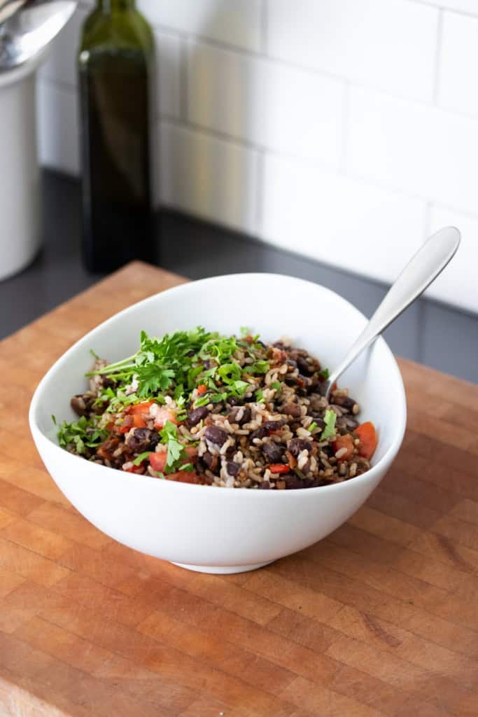 A black bean and rice salad in a white bowl topped with fresh chopped cilantro sitting on a wooden surface.