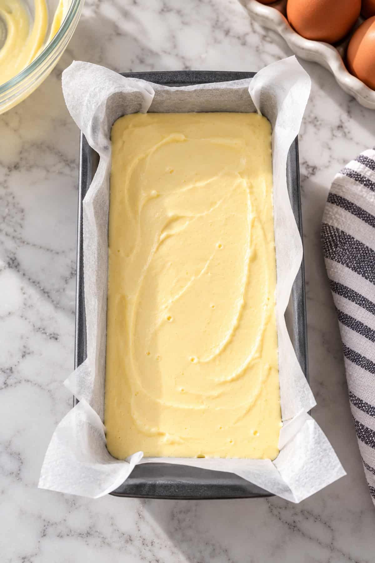 Cheesecake batter added to a baking loaf pan lined with parchment paper.