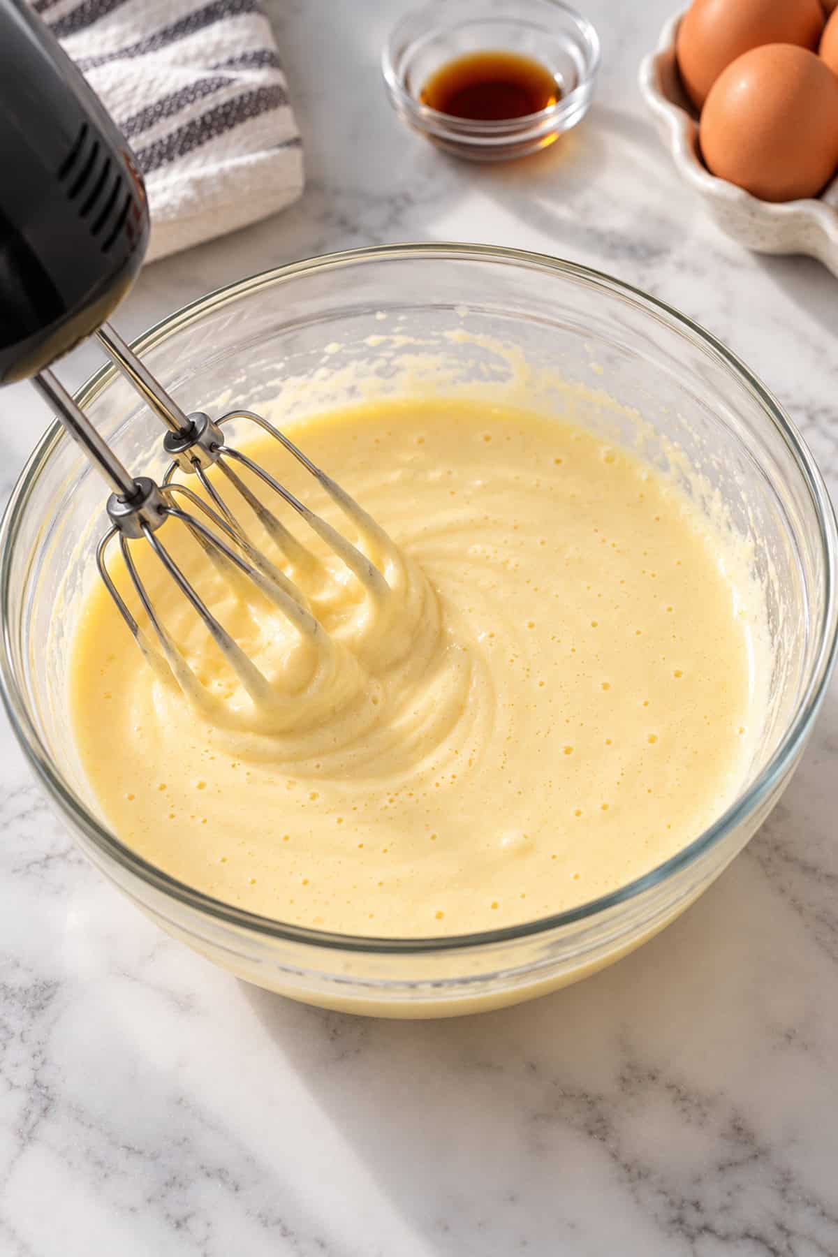 Hand mixer mixing cheesecake batter in a bowl.