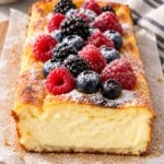Healthy cheecake topped with berries, sliced on a cutting board lined with parchment paper.